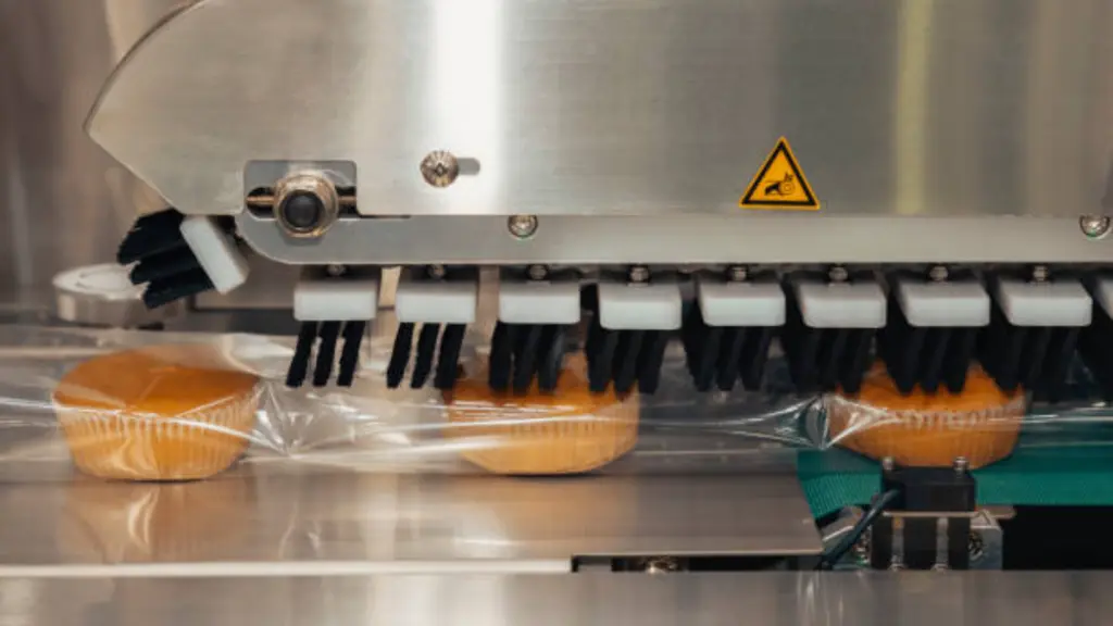 Baked bread in food grade plastic bag on conveyor belt moves to seal in packing machine at production line of bakery manufacturing factory.