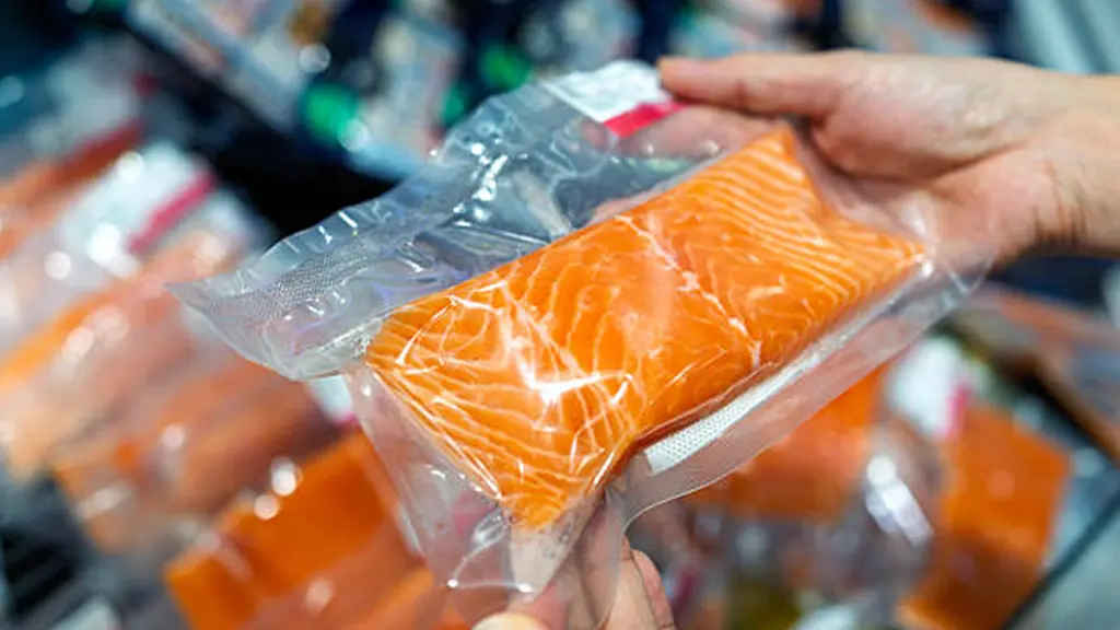 a person's hand holding a packaged fresh raw salmon fillet in a supermarket