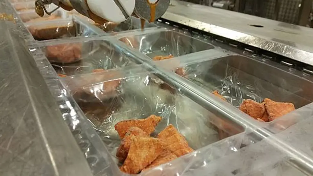 Chicken nuggets in plastic trays being sealed on a conveyor belt