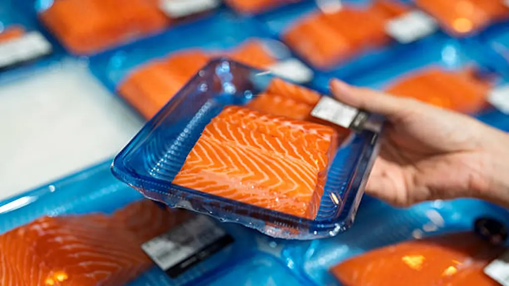 Fresh salmon fillets in sealed blue plastic trays on display.