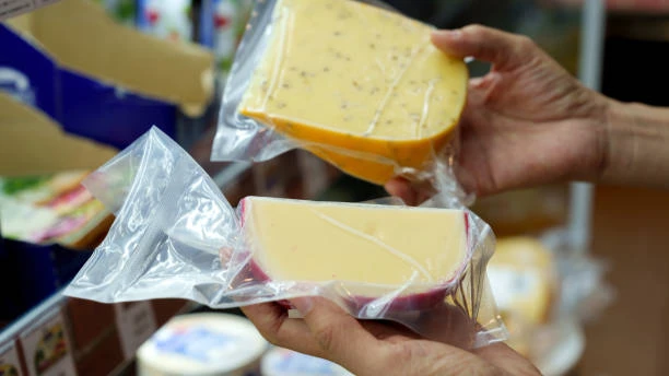 Hands choosing vacuum-packed cheese wedges at the grocery store dairy counter