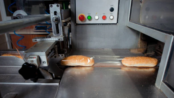 Horizontal flow pack machine wrapping long bread on conveyor belt in automated bakery facility